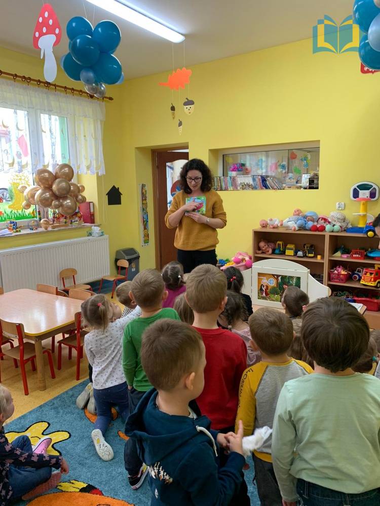 Zdjęcie: Kobieta w przedszkolu pokazuje dzieciom kolorowe książki.